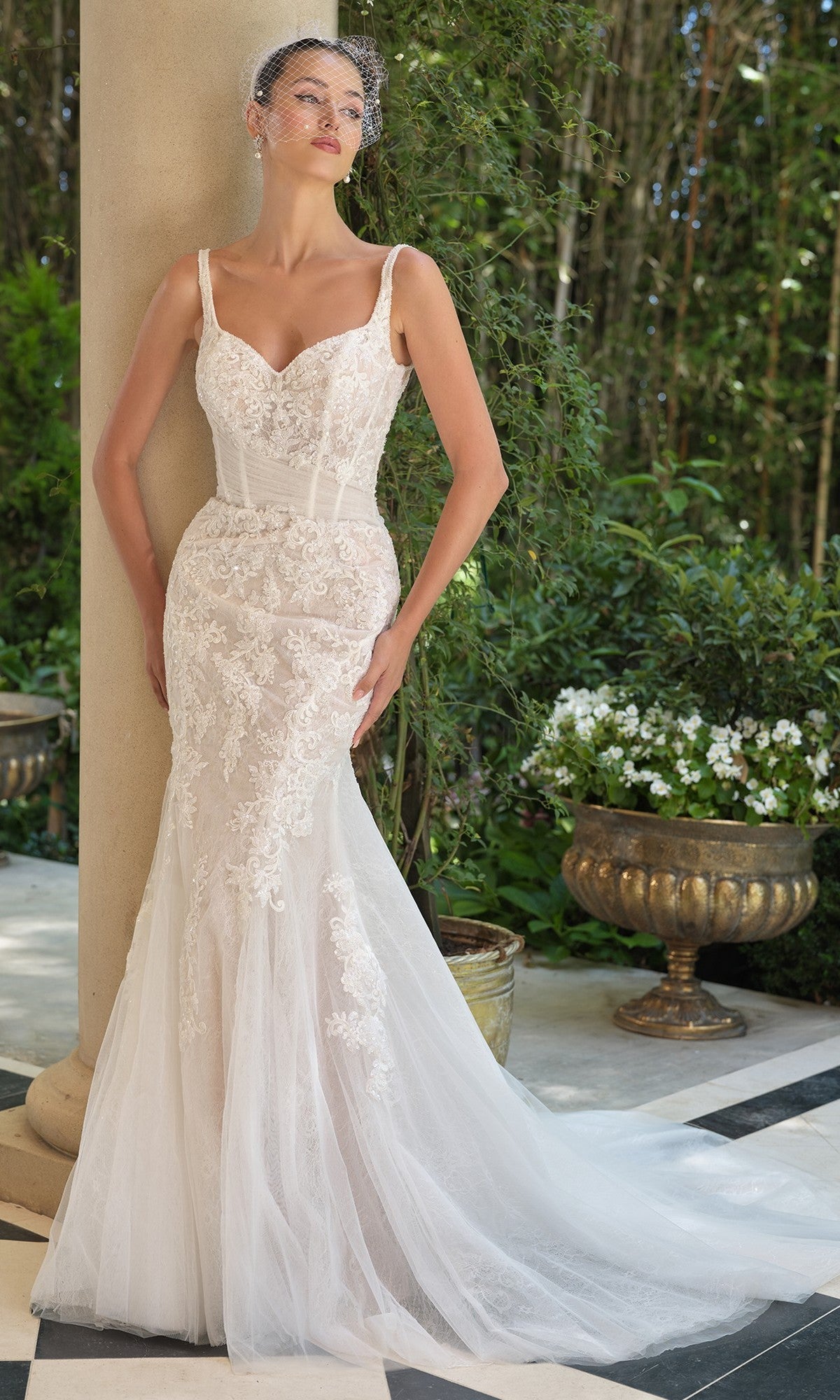 A woman in the Andrea and Leo WL068 long wedding dress with a sheer corset bodice stands by a column in a lush garden.